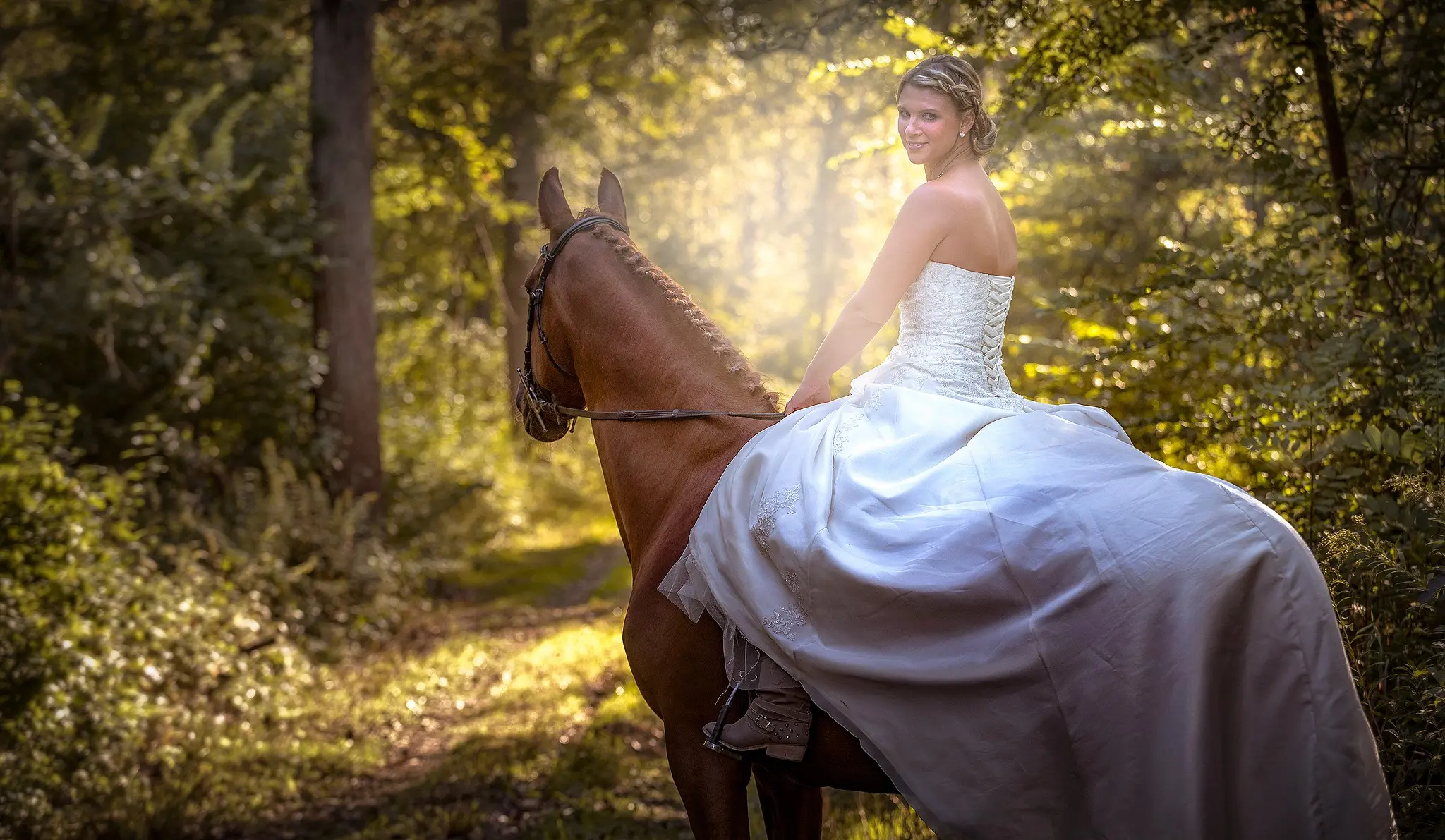 Reiterin im Brautkleid auf einem Braunen im Wald